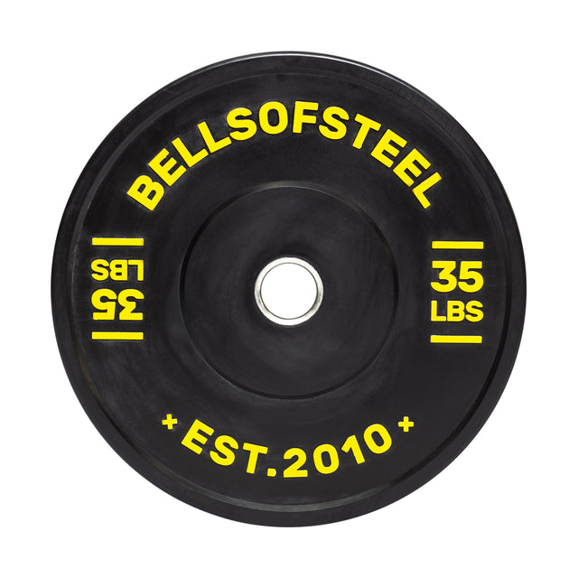 The Dead Bounce Conflict Bumper Plate by Bells of Steel is black with a stainless steel insert, featuring yellow "BELLSOFSTEEL" and "35 LBS" lettering. The durable virgin rubber design also includes "EST. 2010" in smaller yellow text at the bottom.