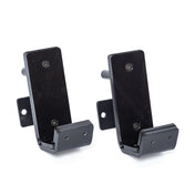 Displayed against a white background are two black metal wall brackets from Bells of Steel, specifically designed for holding or supporting objects. These Standard J-Cups feature a flat top with vertical support and include mounting holes, reminiscent of those commonly used on power racks.