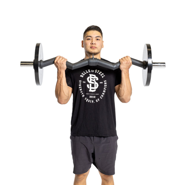 A person wearing a black shirt and shorts showcases impressive grip strength by lifting a Bells of Steel Fat Bar - Olympic Curl Bar Cable Attachment against a plain white background, holding it at shoulder height.