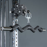 Close-up of the Bells of Steel Fat Bar - Olympic Curl Bar Cable Attachment, a black zigzag-shaped handle connected to gym equipment for strength training and grip improvement. Plain gray background.