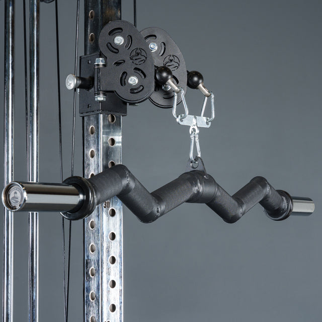 Close-up of the Bells of Steel Fat Bar - Olympic Curl Bar Cable Attachment, a black zigzag-shaped handle connected to gym equipment for strength training and grip improvement. Plain gray background.