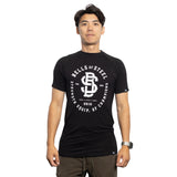 A man faces forward wearing a black Bells of Steel Bamboo T-Shirt, featuring white text and logo, paired with brown pants, set against a plain white background.