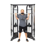 A man stands at a cable machine, holding the Bells of Steel Double Hook Straight Bar Cable Attachment across his shoulders and upper back. He wears a gray t-shirt, black shorts, and black sneakers, facing forward with a neutral expression.