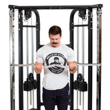 A man in a Bells of Steel t-shirt does a bicep curl with the Double Hook EZ Curl Bar Cable Attachment, positioned centrally for joint-friendly barbell exercises.