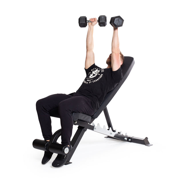 A person in a black T-shirt and pants works out on an adjustable bench, lifting two Bells of Steel Ergo Rubber Hex Dumbbells with ergonomic grips above their chest against a plain white background.