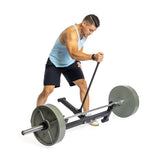 Wearing a light blue tank top and black shorts, an individual exercises with a rowing machine featuring nylon rollers, effortlessly adjusting the weight. They use the machine's handle in a bent-over position, reminiscent of Bells of Steel's Deadlift Jack with Rollers for optimized form.