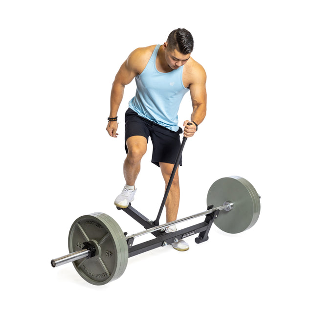 Clad in a light blue tank top and black shorts, an individual steps on the Bells of Steel Deadlift Jack with Rollers, possibly using it to enhance their workout against a plain white background.