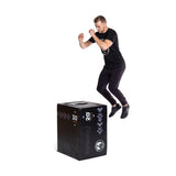 A man in black athletic wear jumps onto the Bells of Steel 6-In-1 Soft Foam Plyo Box/Squat Box, demonstrating this space-saving exercise equipment with multiple height options against a white background.