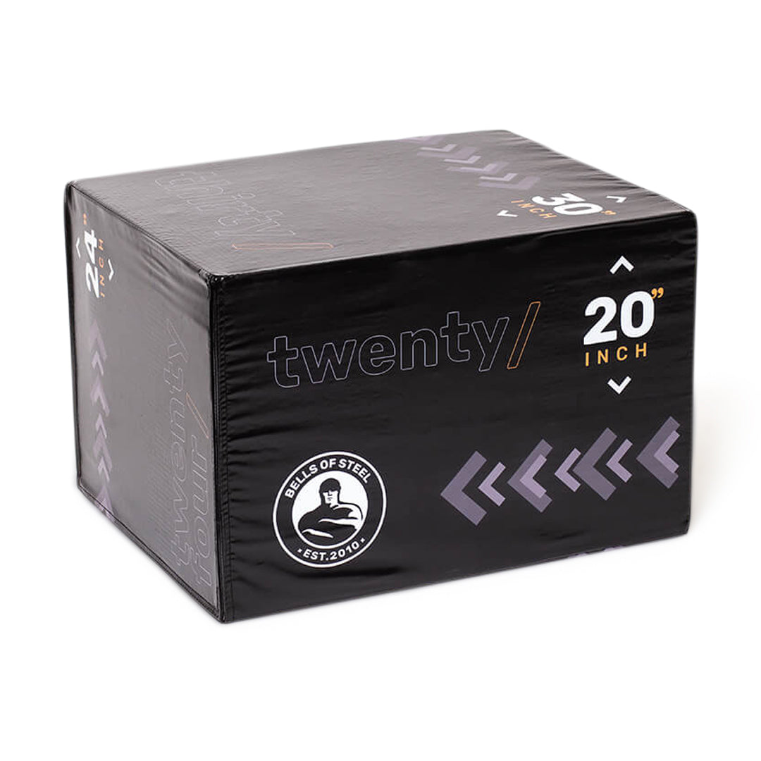 A black box displaying the text "twenty/" and "20 inch," prominently features the Bells of Steel logo with a silhouette lifting weights, encircled by "Bells of Steel Est. 2010." This space-efficient design boasts several arrow-like patterns and is made with a durable synthetic leather shell, as part of the versatile 6-In-1 Soft Foam Plyo Box / Squat Box.