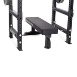 A close-up of a Bells of Steel weight bench inside a power rack featuring Flip-Down Safeties for enhanced training safety, with adjustable holes and attached weight plates.