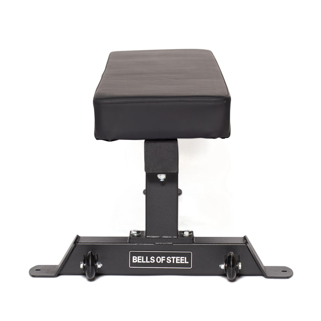 The Powerlifting Flat Bench by Bells of Steel features a flat, black heavy-duty design with a padded surface and a robust metal frame. Crafted for intense training, it includes small wheels at the base for easy mobility. The "Bells of Steel" brand prominently assures quality for powerlifting enthusiasts.