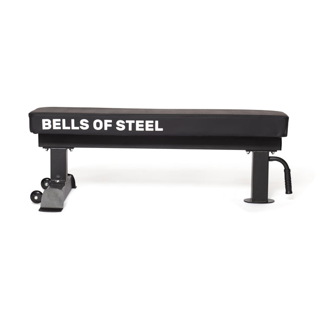 The Powerlifting Flat Bench by Bells of Steel is a black heavy-duty weight bench with a maximum capacity of 1,000 pounds. It features a sturdy metal frame and two small wheels on one end for easy mobility.