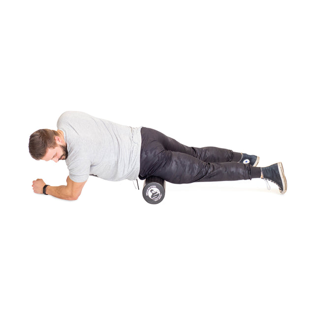 A man in a gray t-shirt and black pants uses the Bells of Steel Foam Roller under his right thigh while lying on his side, supporting himself on his forearms and left leg for effective self-myofascial release.