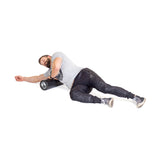 A man uses the Bells of Steel Foam Roller under his shoulder on a white background, wearing a gray t-shirt, black pants, and sneakers, performing a self-myofascial release exercise for post-workout recovery.