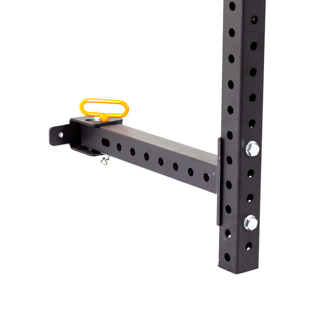 A close-up of a black metal bracket with 5/8" holes is shown attached to a vertical beam in a garage gym. This Bells of Steel Folding Rack 2.3" x 2.3" features a wall-mounted design and includes a horizontal bar with a yellow handle. The bracket is equipped with bolts and a locking pin, providing secure support for up to 600 pounds of static weight capacity.