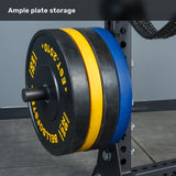 Black, yellow, and blue weight plates are neatly stacked on a horizontal rack attached to the Bells of Steel Manticore Half Rack Builder (3" x 3", 1" Holes) with sturdy 3x3 uprights, set on a gray floor, with the text "Ample plate storage" above.