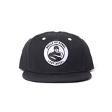 The Bells of Steel Snap Back Hat is a black flat-brim cap with a round white patch on the front, featuring "BELLS OF STEEL EST. 2010" and a kettlebell lifter—perfect for gym enthusiasts seeking style and shade.