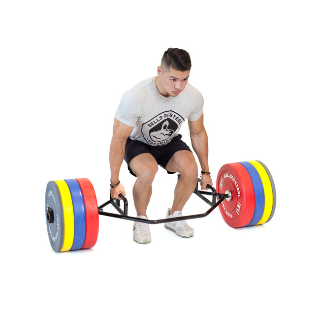 A person in a grey T-shirt and black shorts is executing a deadlift with the Bells of Steel Open Trap Bar / Hex Bar, which features rotating sleeves for smoother motion, loaded with colorful weight plates. The background is plain white.