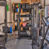 The Hydra Storage Builder by Bells of Steel is a modular home gym featuring kettlebells, a barbell, weights, resistance bands, and a cable machine. Exercise balls and colorful weight plates are neatly organized on shelves for diverse workout routines.