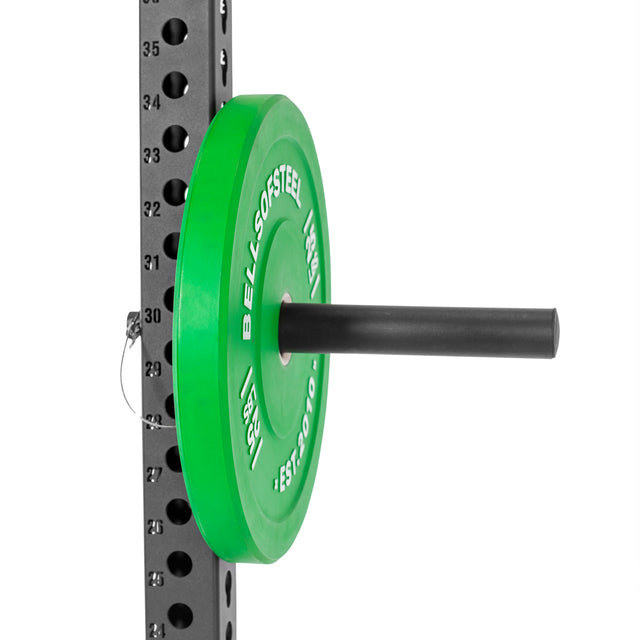 A Bells of Steel Utility Horn Rack Attachment holds a green Olympic weight plate on a vertical storage post with perforations and numbered labels, featuring "BELLS OF STEEL, EST. 2010.