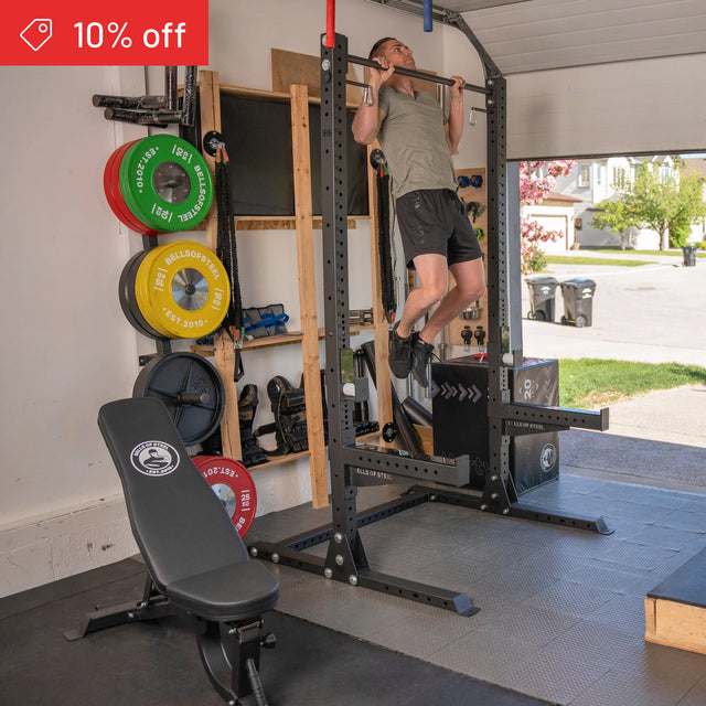 A man uses the Bells of Steel Home Gym Builder power rack in his garage gym, with barbell, bench, and weight plates nearby; a "10% off" sale banner is shown in the upper corner.