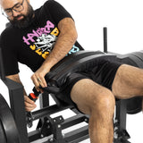 A person wearing a black T-shirt and shorts adjusts a belt while seated on the Bells of Steel Hip Thrust Machine. Set against a white background, they appear focused, ready to tackle their workout.