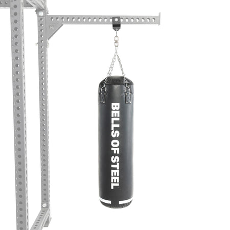 A black Heavy Bag Set from Bells of Steel hangs by chains from a metal Power Rack against a white background.