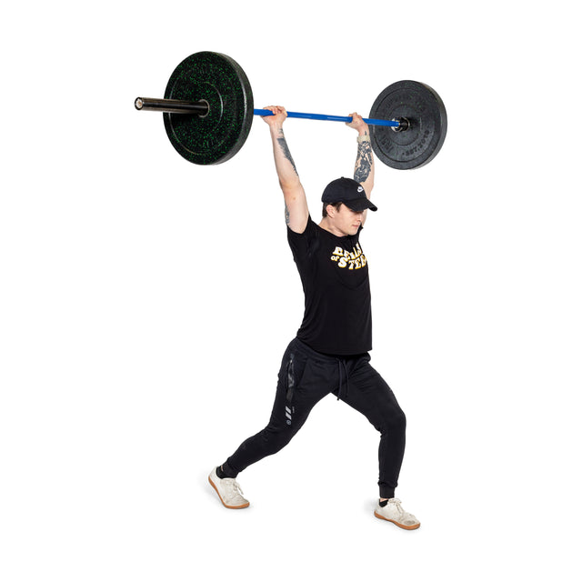 A person lunges powerfully, lifting the Bells of Steel Multi-Purpose Olympic Barbell – The Utility Bar overhead. They wear a black cap, t-shirt, and pants with white sneakers, standing against a plain white background.