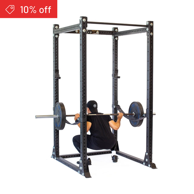 A person in black workout clothes squats with a barbell inside the Bells of Steel Hydra Flat Foot Power Rack Builder (3" x 3", ⅝" Holes), perfect for home gyms. A red "10% off" sale banner appears in the top left corner.