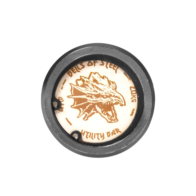 Close-up of a barbell end cap showing a dragon logo and "Bells of Steel" text. The circular, neutral-colored design is rugged, ideal for serious lifters. Product: Multi-Purpose Olympic Barbell – The Utility Bar by Bells of Steel.