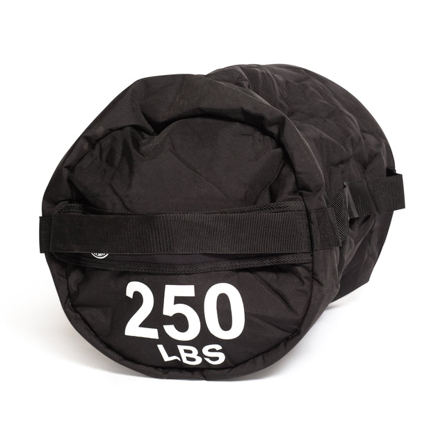 A black Fitness Sandbags by Bells of Steel with a robust Condura construction, prominently displaying "250 LBS" in white lettering, is depicted against a plain white backdrop. The cylindrical bag includes sturdy handles, ideal for sandbag workouts.