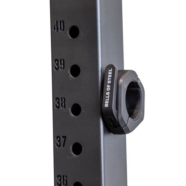 Close-up of a black gym rack upright with numbered holes (36–40) along the side. A Bells of Steel Magnetic Clamp Collar is secured in hole 38.