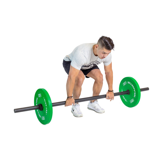 A person in a white T-shirt and black shorts is getting ready to lift the Axle Bars by Bells of Steel, featuring green weight plates. Showing remarkable grip strength, they are bent over with feet shoulder-width apart, hands gripping the bar, all set against a plain white background.