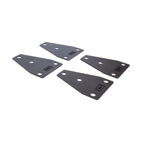 Four black metal Manticore Flat Foot Components by Bells of Steel, each with rounded corners and three holes, are displayed on a white surface. A small logo or text appears in the corner of each component.
