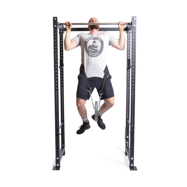 Using the Belt Squat Belt by Bells of Steel, a person performs a pull-up on a bar, wearing a t-shirt, shorts, and sneakers. The belt's durable design allows for extra resistance while maintaining focus.