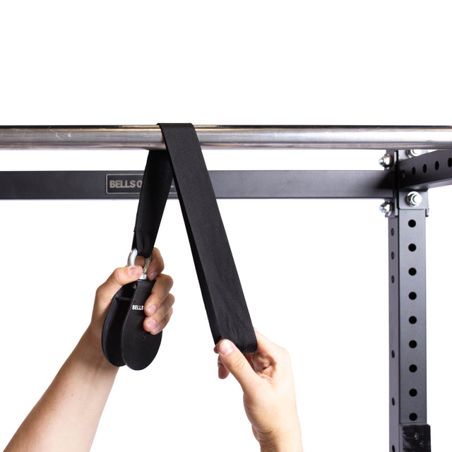 A person demonstrates the Bells of Steel Cable Pulley, effortlessly pulling a strap through the metal frame setup. The gym environment boasts an impressive weight plate capacity, enhancing the workout experience.