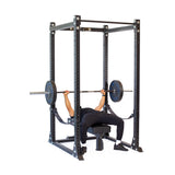 Lying on a bench inside the Bells of Steel Hydra Flat Foot Power Rack Builder (3" x 3", ⅝" Holes), a person confidently performs a barbell bench press with safety straps and Hydra rack attachments against a plain white background.