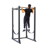 Clad in black athletic wear, an individual performs a pull-up on the Bells of Steel Hydra Flat Foot Power Rack Builder (3" x 3", ⅝" holes) with Hydra attachments. The robust, modular setup has numerous adjustment holes, emphasized against a plain white background.