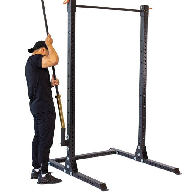 Dressed in black clothing and a cap, a person is optimizing their home gym organization by attaching a Vertical Mount Barbell Holder Rack Attachment from Bells of Steel to a power rack. This setup ensures that everything, including the squat equipment, is neatly arranged inside the gym.