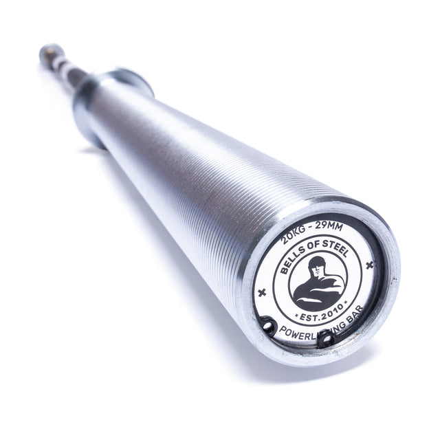 A close-up view of the weighted barbell reveals a logo label on the end cap that says "Bells of Steel, Est. 2010, Powerlifting Bar." Designed for enthusiasts in search of the best budget powerlifting bar, its ridges shimmer along the horizontal length, highlighting its quality craftsmanship.