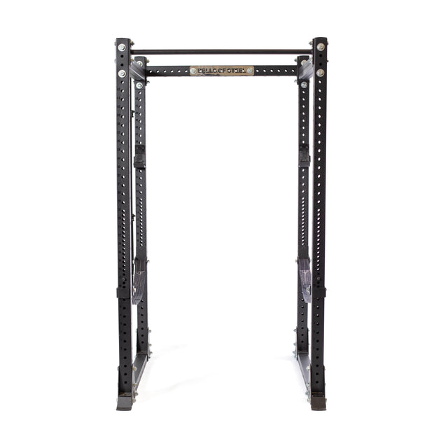 A Bells of Steel Hydra Flat Foot Power Rack Builder (3" x 3", ⅝" holes) in black, with a "Place of PE" sign, features adjustable safety bars and multiple holes for versatile Hydra rack attachments, ideal for weightlifting and strength training.