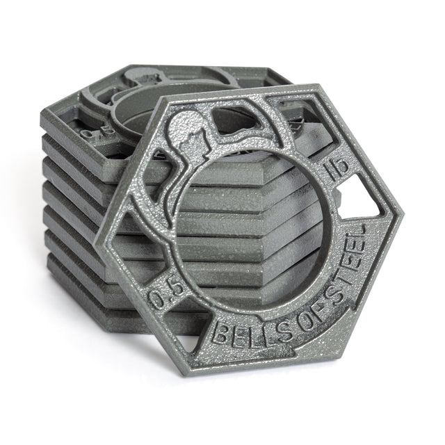 Hexagonal cast iron weight plates with a central hole feature embossed designs, like a kettlebell and "BELLS OF STEEL" text. These Fractional Iron Plates by Bells of Steel have a textured, metallic look.