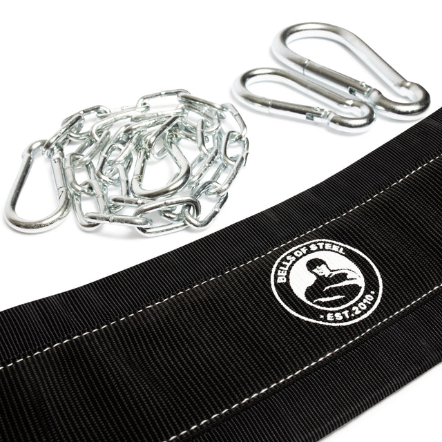 Close-up of a black Belt Squat Belt by Bells of Steel featuring a logo with a muscular figure and "EST 2010" text. Renowned for durability, it includes a metal chain and carabiners, ideal for weighted dips or belt squats on a white background.