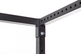 Close-up of a corner joint on the Bells of Steel Residential Power Rack (2.3" x 2.3", ⅝" holes), showing intersecting black metal beams joined by a bolt and nut, with evenly spaced holes along the horizontal beam.