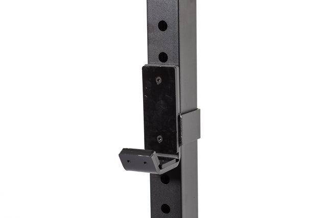 A close-up of a black adjustable metal hook bracket, similar to j-cups, is mounted on the vertical pole of the Bells of Steel Residential Power Rack, featuring multiple ⅝" holes for height adjustment. This simple yet functional design is perfect for home gym setups or shelving within a Power Rack configuration.