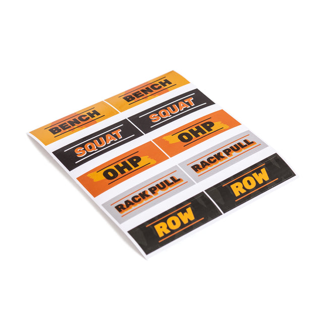 A sheet of durable vinyl die-cut stickers from Bells of Steel displays various weightlifting exercise names, including "BENCH," "SQUAT," "OHP," "RACK PULL," and "ROW" in bold letters on orange and black backgrounds. Enjoy free shipping with every purchase.