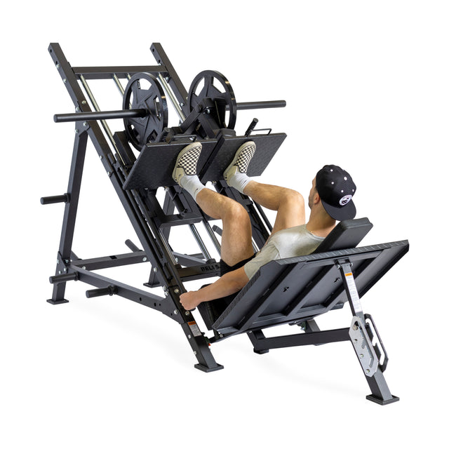 A person in a cap and shorts is using the Bells of Steel 2-in-1 Iso Leg Press & Hack Squat Machine, also known as The Juggernaut, to perform leg presses by pushing weight plates with their feet. This sturdy equipment is ideal for calf raises as well and includes a supportive backrest.