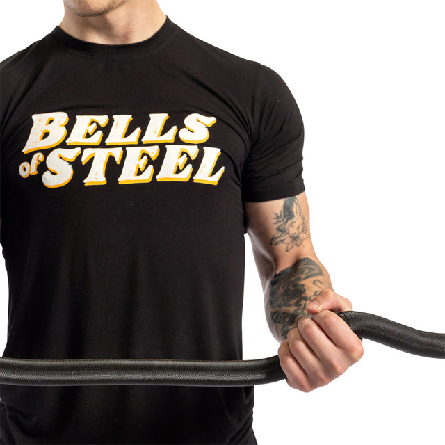 A person grips a battle rope in a "Bells of Steel" t-shirt, showcasing a tattooed arm ideal for biceps and triceps development with the Rackable EZ Curl Bar against a plain white backdrop.