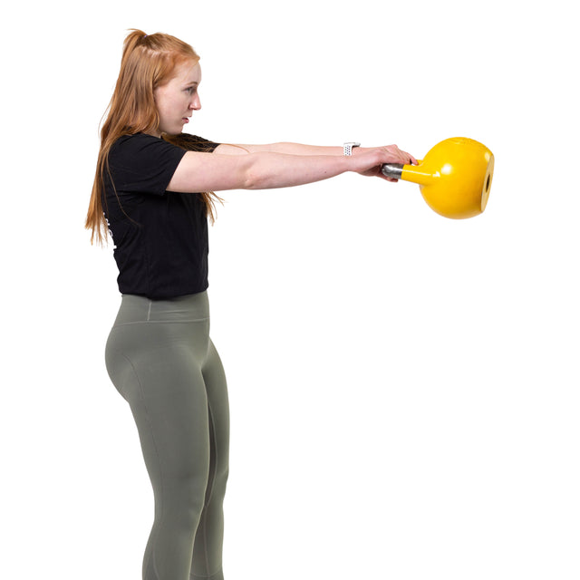 A person with long red hair, dressed in a black shirt and green leggings, executes a kettlebell swing using an ergonomic design yellow Competition Kettlebell from Bells of Steel. The scene captures their side profile against a plain white background, highlighting their commitment to Kettlebell Sport.