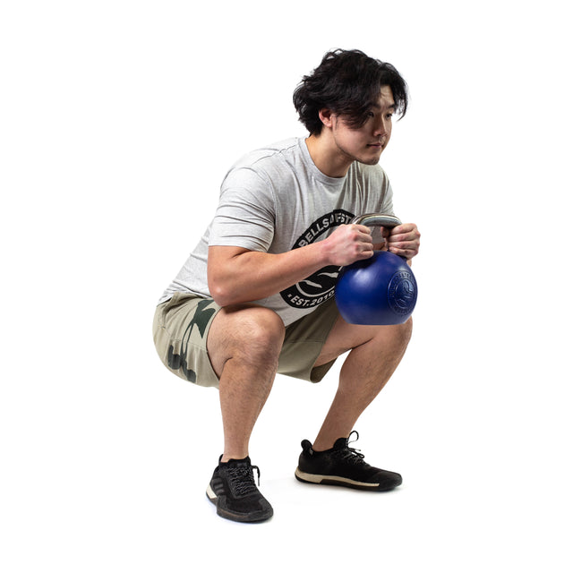 A person dressed in a gray T-shirt and camo shorts executes a squat using the Bells of Steel Competition Kettlebells. They are wearing black athletic shoes while positioned against a plain white background.